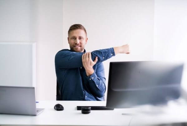 A man sitting in front of his computer, stretching his arm across his body