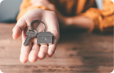 A person's hand holding a house key with a house-shaped keychain.
