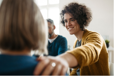 A person smiles while placing a hand on the shoulder of another individual in a group setting.