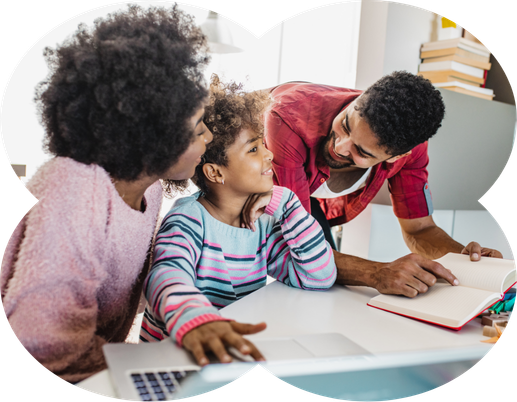 A family sits at a desk, with a woman and a young girl looking at a laptop while a man points to a book.