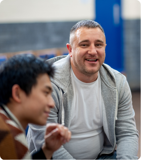 A smiling man in a grey hoodie listening attentively to a colleague during a group discussion.